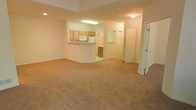 This two-floor residential space offers a thoughtfully designed layout that balances openness with functionality. The main living area is generously sized, featuring warm beige carpeting that creates a cozy and inviting atmosphere. Neutral-toned walls throughout lend a clean, versatile backdrop suited to a variety of interior styles.

The kitchen is positioned at the heart of the main floor and features light wood cabinetry, a built-in microwave, and white appliances. A raised pass-through counter separates the kitchen from the living area, providing both a visual connection and a casual dining or serving surface. Recessed and overhead lighting ensures the space is well-lit throughout.

Adjacent to the main living area, a paneled door leads to additional rooms, offering clearly defined zones for living and private spaces. The layout provides a natural flow between the kitchen, living area, and the rest of the home. Architectural details such as clean white baseboards and panel-style doors add a classic residential character.

Spanning two floors, this space provides ample room for comfortable everyday living, with the multi-level layout allowing for a natural separation between communal and private areas. The overall ambiance is bright, clean, and move-in ready.