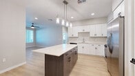 Located at 39695 W Lococo St in Maricopa, AZ, this single-story home offers four bedrooms and two bathrooms within a well-designed, functional layout. The kitchen stands out as a central highlight, featuring crisp white shaker cabinetry, a contrasting dark-based island with a bright white quartz countertop, stainless steel appliances, and modern pendant lighting — all set atop light wood-style flooring that extends throughout the main living areas. The open kitchen flows seamlessly into the living room, which is filled with natural light from a front-facing window and door, and is equipped with a ceiling fan overhead. The four bedrooms are appointed with soft neutral carpet, ceiling fans, and windows with blinds that allow for natural light and privacy. The primary bedroom includes direct access to a dedicated closet. Both bathrooms are finished with light wood-style flooring, white vanity cabinetry with black hardware accents, and clean white fixtures. One bathroom features a walk-in shower with an arched tile surround. Throughout the home, a cohesive neutral color palette, clean white trim, and black hardware details create a contemporary and move-in-ready atmosphere.