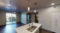 Located at 6811 E Main St in the heart of Scottsdale, Arizona, this thoughtfully designed single-floor residence showcases a contemporary aesthetic throughout. The open-concept kitchen serves as the centerpiece of the living space, boasting a large quartz island with striking marble-like veining, an undermount stainless steel sink with a professional-style coil faucet, and sleek pendant lighting overhead. White upper cabinetry contrasts with gray lower cabinets, while a full suite of stainless steel appliances — including a gas range with microwave, and a French door refrigerator — lines the back wall above a subtle tile backsplash. Herringbone-patterned tile flooring runs throughout the kitchen and living areas, lending a refined, modern touch. The living area connects seamlessly to an outdoor space via a sliding glass door, with a ceiling fan providing comfort. The bedroom offers plush carpeting, a ceiling fan, and a generous window framing views of surrounding greenery. The bathroom features a quartz vanity with a large mirror, gray cabinetry, recessed lighting, and a full tub-shower combination with clean white subway tile detailing. The unit's neutral color palette and quality finishes create a cohesive, move-in-ready environment.