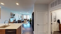 This well-appointed single-floor residence showcases a thoughtfully designed open-concept layout that seamlessly connects the kitchen, dining, and living areas. Dark hardwood flooring runs throughout, providing a warm, cohesive foundation that complements the clean white walls and modern finishes.

The kitchen is a standout feature, outfitted with rich walnut cabinetry, white quartz countertops, and black stainless steel appliances including a side-by-side refrigerator, range, and built-in microwave. A spacious island with bar seating offers an ideal spot for casual dining, while under-cabinet lighting adds a refined touch.

The open living area is bathed in natural light courtesy of large windows with sheer curtains, offering views of the surrounding urban landscape. Recessed lighting throughout enhances the bright, airy ambiance. A louvered closet door adds a classic architectural detail near the entryway.

The bedroom is a serene retreat, featuring a bold green accent wall, large windows, and dark hardwood floors that continue from the main living space, creating a calming and cohesive environment.

The bathroom is finished with a walnut vanity, white quartz countertop, a large mirror, and dark hardware, maintaining the consistent warm-toned, modern aesthetic found throughout the residence.