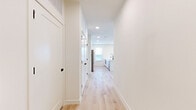 This modern single-floor home in Round Rock, Texas, offers a bright and clean aesthetic defined by white walls, light wood-style flooring, and black hardware accents throughout. A wide hallway with recessed lighting and Shaker-style doors leads into the open-concept kitchen and living area. The kitchen is a standout feature, boasting sleek white cabinetry, a wall-mounted range hood, stainless steel appliances including a French door refrigerator, and a large white island with a matte black sink faucet — ideal for both cooking and entertaining. The living area provides an abundance of natural light through multiple windows and includes direct access to an outdoor area via a glass-panel door. Both bedrooms are well-proportioned and feature light wood flooring, large windows with exterior views, and ceiling fans for added comfort. The spacious primary bedroom connects to an en-suite bathroom equipped with a glass-enclosed walk-in shower, a double vanity with white cabinetry, and a walk-in closet. A secondary bathroom features full-height tile surrounding a soaking tub and shower combination with matte black fixtures. A dedicated laundry area with built-in cabinetry and a window completes the thoughtfully designed layout.