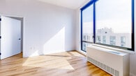 Located on the 15th floor at 69-02 Queens Blvd in Woodside, NY, this modern 2-bedroom, 2-bathroom residence offers a well-designed layout with clean contemporary finishes throughout. Warm-toned hardwood flooring runs continuously across the living spaces, complementing the crisp white walls and creating a bright, cohesive aesthetic.

The open kitchen features a central island with a quartz-style countertop, sleek flat-front white cabinetry extending to the ceiling, stainless steel appliances including a full-size refrigerator and range, and a matte black faucet at the undermount sink. The adjacent living area provides an open, flexible space with direct sightlines to the kitchen.

Both bedrooms are well-proportioned and filled with natural light. The primary bedroom is generously sized and includes a large sliding closet. Floor-to-ceiling black-framed windows in the bedrooms frame sweeping views of the Queens skyline, with abundant sunlight pouring in throughout the day.

The two bathrooms are finished with large-format porcelain tile, light wood vanities, matte black fixtures, and soaking tubs with fully tiled surrounds. A hallway connects the bedrooms and bathrooms, and two closets provide practical storage. The overall design is modern, minimalist, and move-in ready.