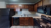 This two-bedroom, one-bathroom unit is arranged on a single floor, offering a practical and comfortable layout. The kitchen serves as a central feature, outfitted with rich dark-wood cabinetry extending to the ceiling for ample storage, granite-style laminate countertops, a double stainless steel sink, and a full suite of black appliances including a refrigerator, electric range, dishwasher, and over-the-range microwave. A peninsula counter separates the kitchen from the adjacent living area, creating an open, connected feel. The living room is generously sized with plush carpeting, a large sliding glass door that invites natural light, and baseboard heating along with a wall-mounted air conditioning unit. Both bedrooms feature soft carpeting, textured ceilings, individual windows with natural light, and baseboard heaters. The full bathroom is finished with stone-look tile flooring, a white tub-shower combination with a handheld showerhead, a wood-vanity with a light countertop, and a wall mirror. Throughout the unit, neutral taupe wall tones and consistent finishes create a cohesive, move-in-ready atmosphere.