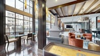 Located at 4020 Koehler Street in Houston's vibrant River Oaks/Washington Corridor neighborhood, this generously sized amenity clubroom is a standout social hub defined by dramatic architectural design and upscale finishes. The space is anchored by soaring double-height ceilings, floor-to-ceiling steel-framed windows that flood the interior with natural light, and direct views of the resort-style pool courtyard beyond.

Rich hardwood flooring transitions seamlessly into plush area rugs, delineating distinct zones throughout the open-plan layout. A central freestanding fireplace serves as a striking focal point, while exposed wood beam ceilings and an eye-catching geometric lattice ceiling installation add layers of texture and visual interest.

The lounge area features plush rust-orange swivel chairs and teal sofas arranged around a glass coffee table, complemented by a built-in upholstered window bench with accent pillows. A dedicated game zone includes a foosball table, shuffleboard, and billiards table beneath designer pendant and chandelier lighting. A bar area with counter seating and a media wall with a large flat-screen TV round out the entertainment offerings.

The space is further elevated by curated artwork, sculptural light fixtures, and a cohesive contemporary-meets-warm-industrial aesthetic that makes it equally suited for casual socializing or community gatherings.