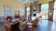 This single-story clubhouse in Ypsilanti, Michigan, is designed to serve as a refined communal gathering space with a warm, traditional aesthetic throughout. The centerpiece of the facility is a grand great room boasting dramatically high coffered ceilings, dark hardwood floors, and a floor-to-ceiling stone fireplace topped with a decorative sailboat sculpture. Tall arched windows and full-length glass doors flood the space with natural light while framing outdoor views, and plaid drapery adds a classic, tailored touch. An ornate iron chandelier hangs above generously arranged patterned sofas and armchairs, creating an inviting atmosphere for socializing.

Adjacent seating areas offer additional lounge space with leather sofas, arched windows overlooking outdoor amenities, and a coffered ceiling detail that maintains architectural consistency. A fully equipped kitchen features rich wood cabinetry, dark granite countertops, stainless steel appliances, travertine tile flooring, and a breakfast bar with leather-upholstered stools. A dining area accommodates group gatherings around a solid wood table. The dedicated business center includes built-in wood shelving, a workstation, and a conference-style table, providing practical workspace for residents.