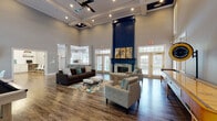 The Country Walk Clubhouse at 2300 Country Walk in Snellville, GA, offers a thoughtfully designed single-floor community space that blends comfort, functionality, and modern style. The centerpiece of the clubhouse is a dramatic grand lounge featuring soaring ceilings with exposed white beams and coffered detailing, rich hardwood-style flooring, and a striking floor-to-ceiling navy blue fireplace surround with a brick hearth. Multiple seating arrangements, including plush sofas and upholstered chairs, create an inviting atmosphere bathed in natural light from large French doors and transom windows that open to the outdoors. A shuffleboard table adds a recreational touch to the lounge area. The fully equipped kitchen features crisp white shaker cabinets, subway tile backsplash, quartz countertops, stainless steel appliances, and gold-accented hardware. A bright dining area accommodates residents with round white tables, modern molded chairs, a wall-mounted television, and a contemporary globe chandelier. The business center offers a clean, functional workstation with dual computer terminals set against a white subway tile accent wall with wooden shelving. Additional spaces include a seating nook and a waiting area with a glass-paned French door, completing this versatile and welcoming community hub.