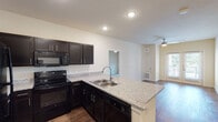 This single-floor residence offers a well-designed, open-concept layout that seamlessly connects the kitchen and living areas. The kitchen is a standout feature, equipped with dark espresso cabinetry, granite countertops, a peninsula with a double-basin sink, and black appliances including a refrigerator, range, microwave, and dishwasher. Rich hardwood-style flooring runs throughout the main living areas, adding warmth and continuity to the space.

The living area is generously sized and benefits from natural light streaming through a set of glass French doors that open to an outdoor space. A ceiling fan provides additional comfort to the room. A hallway connects the main living space to the private areas of the residence.

The bedroom is carpeted for comfort and features a ceiling fan, a window with blinds, and access to a spacious walk-in closet outfitted with dual hanging rods and shelving. The bathroom includes a full tub and shower combination with a curved curtain rod, hardwood-style flooring, dark cabinetry with granite countertops, and a safety grab bar.

A dedicated laundry area houses a full-size, top-loading washer and dryer set along with overhead shelving for additional storage. A water heater is also conveniently located within this utility space.