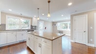 Located at 14 Bliss Ave, this thoughtfully updated 3-floor home blends classic architectural character with modern renovations. The heart of the home is a beautifully designed kitchen featuring white shaker-style cabinetry, a granite-topped center island with beadboard paneling, gray subway tile backsplash, stainless steel appliances including a gas range, microwave, dishwasher, and refrigerator, and pendant lighting over the island. Multiple windows flood the kitchen and adjacent dining area with natural light and views of the surrounding greenery. Rich hardwood flooring flows throughout the main and upper levels, complemented by crown molding and clean white trim. Generously sized rooms offer ample natural light through double-hung windows, and classic cast-iron radiators provide warmth throughout. The bathrooms are well-appointed — one features a tiled tub-shower combination with a dark espresso vanity, while another showcases a glass-enclosed walk-in shower with white subway tile and a mosaic accent border. The upper level includes a charming room with sloped ceilings and a large window overlooking mature trees. The lower level houses a dedicated laundry area with a stacked washer and dryer unit, adding everyday convenience to this well-rounded home.