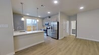 This two-story home is thoughtfully laid out across two floors, with the more expansive main level housing the open-concept kitchen and living area, and the upper level dedicated to the bedrooms and bathrooms. The main floor features light wood-style flooring throughout, creating a bright, cohesive feel. The kitchen is equipped with stainless steel appliances, including a refrigerator, range, and microwave, complemented by gray shaker-style cabinetry, a white quartz countertop peninsula, and recessed lighting with pendant fixtures. A sliding glass door leads directly to a fenced outdoor area, allowing natural light to fill the space. The front entry features a paneled white door with a transom window, alongside a large window that floods the foyer with additional natural light. Upstairs, the three bedrooms are carpeted and well-lit, each with ceiling fans and windows offering neighborhood views. The primary bedroom includes a dedicated walk-in closet with built-in shelving. The primary bathroom offers a gray vanity with white countertops, a tiled walk-in shower, and modern chrome fixtures. Additional bathrooms feature tub-shower combinations with clean subway tile surrounds. Two closets provide ample storage throughout the home.