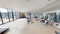 Located at 930 Blue Mound Lane in Huntsville, Alabama, this single-floor fitness center offers a well-appointed and thoughtfully designed workout facility. The space is bathed in natural light, courtesy of expansive floor-to-ceiling glass doors and windows that line one full wall, providing direct views of an outdoor pool and patio area with lounge seating — creating a bright, open atmosphere conducive to an energizing workout experience.

The fitness center is equipped with a comprehensive selection of exercise equipment to support a full range of training needs. Cardio options include multiple elliptical trainers and a treadmill, while strength training is served by a multi-station cable machine, a power rack, adjustable benches, and various free weights including kettlebells. A large wall-mounted mirror spans one side of the room, enhancing the sense of space and providing visual feedback during exercise.

The interior maintains a clean, neutral aesthetic with light-toned carpet flooring, white walls, and recessed lighting throughout the ceiling. A wall-mounted flat-screen television adds a modern convenience to the space. The entrance features a glass-paneled door, and the overall layout is open and spacious, allowing ample room to move between equipment. This facility provides a complete, community-oriented fitness environment with seamless indoor-outdoor connectivity.