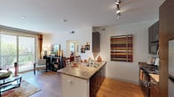 This single-floor residence offers a thoughtfully designed open-concept layout that seamlessly connects the kitchen, dining, and living areas. The kitchen is outfitted with dark espresso cabinetry, granite-style countertops, stainless steel appliances including a full-size refrigerator, a gas range, and a built-in microwave. Track lighting overhead highlights the space, while a peninsula with a double sink and bar seating provides an ideal spot for casual dining. Hardwood-style flooring flows throughout the main living areas, adding warmth and continuity to the open floor plan. The living room is bright and inviting, anchored by a sliding glass door that opens onto a private balcony, allowing natural light and outdoor views to fill the space. The bedroom is generously sized, featuring plush carpeting, a ceiling fan, and large windows that invite abundant natural light. A private door off the bedroom provides additional access. The bathroom is finished with stone-look tile flooring, a dark-cabinet vanity with a large mirror, and a shower. An in-unit washer and dryer is conveniently located adjacent to the bathroom, adding everyday practicality to this well-rounded residence.