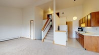 This thoughtfully designed single-floor unit offers a comfortable and functional layout across several well-defined spaces. The heart of the home is a generously sized living room with soaring vaulted ceilings, a ceiling fan, and large sliding glass doors that open onto a private balcony deck, filling the space with natural light and providing pleasant outdoor views of surrounding greenery. A secondary window further enhances the bright, airy atmosphere, while baseboard heating and a wall-mounted heater ensure year-round comfort.

The galley-style kitchen is efficiently arranged with warm wood cabinetry, ample counter space, a double stainless steel sink, and white appliances including a refrigerator and gas range. A dedicated door leads to additional storage or utility access.

The carpeted bedrooms are quiet and spacious, each featuring neutral walls and wood-trimmed sliding closet doors with built-in shelving and hanging rods. Large windows in the bedrooms invite natural light and views of mature trees outside.

A central staircase with a wood handrail and white balusters connects the main living level to additional areas, with a louvered utility closet nearby. The bathroom is clean and functional, featuring a full soaking tub with tiled surround and chrome fixtures. Throughout the unit, soft carpeting, warm wood trim, and a neutral color palette create a cohesive and welcoming environment.