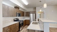 Located at 2411 E Riverside Dr in Eagle, Idaho, this single-floor residence offers a thoughtfully designed layout with contemporary finishes throughout. The kitchen is a standout feature, showcasing rich wood-toned cabinetry that extends to the ceiling for ample storage, bright white quartz countertops, a tile backsplash, and a full suite of stainless steel appliances including a gas range, over-the-range microwave, and a French door refrigerator. Wood-look luxury vinyl plank flooring runs through the kitchen and main living areas, adding warmth and visual continuity. A peninsula with a double basin sink provides additional prep space and casual seating potential. The bedroom is carpeted for comfort and includes a ceiling fan, a window with blinds for natural light control, and a closet. The bathroom features matching wood-toned cabinetry, a vanity with a mirror, and wood-look flooring consistent with the rest of the home. A dedicated laundry area accommodates a full-size top-loading washer and dryer, with built-in shelving overhead for storage. A secondary full bathroom with a tub/shower combo completes the space. The overall aesthetic is clean, modern, and functional.