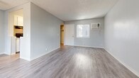 This single-floor, 2-bedroom, 1-bathroom unit offers a clean and functional layout with a neutral color palette throughout. The living room features smooth gray laminate wood flooring, large windows that invite natural light, and a textured ceiling. A ceiling fan adds practicality, and an open sightline connects to the kitchen area, enhancing the sense of space. The kitchen is partially divided from the living area by a half-wall, providing definition while maintaining an open feel. Both bedrooms are carpeted and feature vertical blind-covered windows that allow natural light to filter in. The primary bedroom includes a double sliding-door closet with built-in hanging rods, offering generous storage. The second bedroom also includes a dedicated closet with a hanging rod, making it well-suited as a guest room or home office. A hallway connects the main living areas to the bedrooms and bathroom, providing a logical and efficient flow. The bathroom is finished with wood-look flooring and a full tiled tub-shower combo in white, keeping the space bright and easy to maintain. Throughout the unit, consistent gray-toned walls and white trim create a cohesive, modern aesthetic. Windows throughout the unit provide outdoor views and ventilation, contributing to a light and airy ambiance.