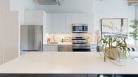 Located at 685 Richmond St in downtown London, Ontario, this thoughtfully designed 2-bedroom, 1-bathroom unit blends modern finishes with an industrial aesthetic. The kitchen is a standout feature, showcasing floor-to-ceiling white cabinetry, a large waterfall-edge island, stainless steel appliances including a range, microwave, and refrigerator, and light hardwood flooring that runs throughout the space. Exposed ductwork and linear track lighting along the ceiling add an urban, loft-like character to the open layout. The primary bedroom is a calm retreat with soaring ceilings, double closets with matte black hardware, and a large window framing views of the London skyline. The second bedroom is a compact, bright room with clean white walls and the same warm hardwood flooring. The bathroom is finished in neutral tones, featuring full-height tile surround in the tub/shower, light wood-look flooring, and a sleek floating vanity. Throughout the unit, a consistent palette of whites, warm woods, and black accents creates a cohesive, contemporary ambiance well-suited to urban living.
