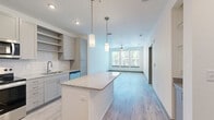 Located at 1050 Beckoning Blvd in Charlotte, NC, this well-appointed one-bedroom, one-bathroom residence offers a thoughtfully designed single-floor layout that maximizes functionality and comfort. Light-toned hardwood flooring flows throughout the main living areas, lending a clean, modern aesthetic to the space.

The open-concept kitchen and living room serve as the heart of the home. The kitchen is outfitted with gray shaker-style cabinetry, white subway tile backsplash, granite countertops, stainless steel appliances — including a refrigerator, range, microwave, and dishwasher — and a central island with pendant lighting above, ideal for casual dining or meal prep. The living area beyond benefits from a bank of large windows that frame lush greenery and fill the space with natural light, complemented by a ceiling fan overhead.

The spacious bedroom continues the bright, airy feel with three generous windows, a ceiling fan, and light hardwood flooring. A dedicated closet provides ample storage. The bathroom features gray cabinetry with granite countertops, a large mirror, tile flooring, and a full tub/shower combination with tiled surround. A separate in-unit laundry area houses a full-size Whirlpool washer and dryer with overhead shelving, adding everyday convenience to this well-rounded residence.