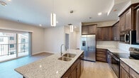 Located at 1500 SW Aileron Cir in Bentonville, Arkansas, this thoughtfully designed 2-bedroom, 2-bathroom home offers a comfortable and modern living experience on a single floor. The open-concept kitchen serves as the heart of the home, showcasing a large center island with a double undermount sink and striking granite countertops. Rich dark-stained cabinetry, a white subway tile backsplash, and a full suite of stainless steel appliances — including a French door refrigerator, range, microwave, and dishwasher — complete the space. Pendant lighting above the island adds a stylish touch, while recessed lighting throughout ensures a bright and welcoming atmosphere. Light-toned luxury vinyl plank flooring flows seamlessly through all rooms, complementing the neutral, warm-toned walls. Both bedrooms are generously proportioned, each featuring ceiling fans and clean-lined panel doors. The primary bedroom benefits from a walk-in closet with built-in shelving. The secondary bedroom includes a window offering natural views of the surrounding area. Both bathrooms mirror the home's refined aesthetic, featuring granite-topped vanities with dark cabinetry and large mirrors. A dedicated closet with additional shelving provides ample storage throughout this well-organized, move-in-ready home.