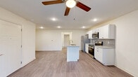 Located at Compass Flats Court in Lafayette, Indiana, this well-appointed one-bedroom, one-bathroom residence offers a comfortable and functional single-floor layout. The open-concept kitchen and living area serves as the heart of the home, highlighted by a large granite-topped island with an integrated sink, crisp white shaker cabinetry, a stylish tile backsplash, and a full suite of stainless steel appliances including a refrigerator, gas range, and over-the-range microwave. Light wood-tone flooring runs throughout the main living area, complementing the neutral warm-white walls and recessed lighting. The living room is generously sized, featuring a ceiling fan with light fixture and direct access to a private outdoor balcony through a set of glass-paneled French doors, bringing in natural light and outdoor views. The bedroom offers plush carpeting, a natural light-filled window, and access to a dedicated closet. The full bathroom is clean and functional, appointed with a full soaking tub and shower combination with polished chrome fixtures and wood-look flooring. A dedicated in-unit laundry room houses a full-size washer and dryer alongside built-in wire shelving for added storage. The overall ambiance is modern, clean, and move-in ready.
