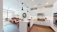 This thoughtfully designed single-floor residence showcases a seamless blend of modern aesthetics and functional living. The heart of the home is a chef-inspired kitchen featuring floor-to-ceiling white cabinetry, a classic subway tile backsplash, and a suite of stainless steel appliances including a gas range, double wall ovens, and a French door refrigerator. A generous island with a quartz countertop and an undermount sink provides both prep space and casual seating, while pendant lighting adds a stylish accent overhead. The kitchen flows naturally into the open living and dining area, where warm hardwood flooring and large floor-to-ceiling glass doors invite abundant natural light and direct access to an outdoor space with palm tree views. The living room offers a relaxed yet refined atmosphere. The primary bedroom is a tranquil retreat with a tray ceiling, hardwood flooring, and a window framing outdoor views. A second bedroom provides comfortable accommodations with soft neutral tones. Two well-finished bathrooms serve the home — one featuring a walk-in glass shower and the other a full soaking tub — both appointed with warm wood vanities, white quartz countertops, and large-format tile flooring.