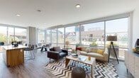 This contemporary single-floor residence is defined by its bold architectural design and an abundance of natural light. The expansive living area is anchored by floor-to-ceiling glass windows that frame sweeping urban views, including glimpses of a nearby outdoor pool and city skyline. The open layout flows seamlessly between a stylishly furnished lounge space and a dedicated dining area, both benefiting from the dramatic glass façade. Rich hardwood-style flooring runs throughout, complementing the clean, modern aesthetic.

The kitchen features a refined two-tone cabinetry design — warm natural wood on the lower cabinets paired with deep taupe uppers — along with stainless steel appliances, a subway tile backsplash, and ample counter space. The bedrooms are generously proportioned, each with large windows that invite natural light and connect to the urban surroundings. One bedroom showcases a stylish sliding barn door leading to a walk-in closet with dual clothing rails. Bathrooms are finished to a high standard, featuring wood-framed vanity mirrors, quartz countertops, and tile-surround soaking tubs or walk-in glass-enclosed showers. A spacious walk-in closet provides excellent storage. The overall ambiance is sleek, bright, and urban.