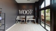 Located in Charleston, SC, this single-floor pet grooming facility is designed with both functionality and style in mind. The space makes a strong first impression through its grand entrance, featuring soaring floor-to-ceiling glass windows and double glass doors that flood the entryway with natural light, set against dark-painted walls and clean white tile flooring.

The grooming area is a standout feature, anchored by two stainless steel professional dog wash tubs positioned beneath a bold "WOOF" wall graphic — a striking design detail that adds personality to the space. Large windows alongside the wash stations bring in ample natural light and provide views of the surrounding streetscape. Each tub is equipped with a handheld sprayer and step stool for ease of use.

The grooming room continues the dark-and-light aesthetic with charcoal-toned walls contrasted by bright white tile floors. A professional grooming table with adjustable arm, a multi-tier metal shelving unit stocked with grooming supplies, baskets, and folded towels, and a stainless steel grooming tub round out the well-equipped workspace. The open layout allows groomers to move freely and efficiently throughout the room. Overall, the facility presents a clean, professional, and thoughtfully designed environment purpose-built for pet care services.