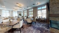 Located at 45 Coburg Rd in Charleston, South Carolina, this sophisticated single-story community facility offers a refined blend of modern design and welcoming comfort. The grand entrance lobby immediately impresses with soaring double-height ceilings, floor-to-ceiling glass double doors, sheer drapery panels, and an abundance of natural light. Tall potted fiddle-leaf fig trees flank the entryway, while plush seating arrangements on richly patterned carpeting create an inviting reception area.

The expansive lounge features dramatic ceiling height, large clerestory windows, a statement sculptural chandelier, and direct access to an outdoor pool area through glass-paneled doors. A large-screen television and cozy seating arrangements make this an ideal gathering space.

The formal dining room is lined with generous windows offering views of the lush surroundings, illuminated by modern circular chandeliers above elegantly upholstered dining chairs and dark wood tables.

A well-appointed kitchenette includes sleek quartz countertops, warm wood cabinetry, a stainless steel appliance suite, and a glossy tile backsplash with metallic accents.

Connecting hallways are tastefully decorated with bold abstract artwork in gilded frames, built-in cabinetry, and intimate seating alcoves adorned with textured stone accent walls, ensuring a polished and cohesive aesthetic throughout.