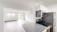 Located at 495 Laurel Hill Rd in Norwich, CT, this three-bedroom, one-bathroom residence offers a clean, contemporary aesthetic across a single floor. Light wood flooring runs throughout, complementing the bright white walls and creating a cohesive, airy atmosphere.

The open-concept living room is generously sized, filled with natural light from large windows and a sliding glass door that leads to a private balcony overlooking lush, tree-covered surroundings — a standout feature of the space. A wall-mounted sconce and a view into the kitchen reinforce the open, connected layout.

The galley-style kitchen is well-appointed with stainless steel appliances including a range, over-the-range microwave, refrigerator, and dishwasher. Sleek gray countertops contrast neatly against crisp white cabinetry, and a window above the sink brings in natural light.

The primary bedroom is a spacious retreat, while the two additional bedrooms each feature warm wood flooring, baseboard heating, and natural light from multiple windows — one offering a brick exterior view. One bedroom includes a built-in closet with shelving.

The bathroom is clean and functional, featuring a full tub-shower combination with chrome fixtures and a privacy window. Baseboard heating is present throughout the home, ensuring year-round comfort.