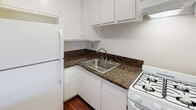 Located at 18014 Sherman Way in the Reseda neighborhood of Los Angeles, this single-floor unit offers a well-organized layout with a cohesive design throughout. Rich, dark hardwood flooring runs continuously across the living areas, providing a warm and polished foundation that complements the neutral-toned walls and textured ceilings.

The open-concept living area is bright and airy, benefiting from a large window that invites natural light and provides an outward view. A wall-mounted air conditioning unit ensures year-round climate comfort. The space flows naturally into the kitchen, which is partially separated by a peninsula counter finished with dark granite-patterned countertops — ideal for casual dining or additional prep space.

The kitchen is well-appointed with white cabinetry offering ample upper and lower storage, matching white appliances including a gas range and full-size refrigerator, a stainless steel sink, and an overhead ventilation hood. The granite-style countertops carry a consistent design language that is echoed in the bathroom vanity.

The bathroom features a white vanity with dark granite-style countertops, a large mirror, recessed storage cabinetry, and modern lighting fixtures above. The same hardwood flooring extends into the bathroom, maintaining a unified aesthetic throughout the unit. A hallway with an additional window provides natural light at the entry of the space.