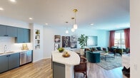 Located at 195 Steely in Irvine, California, this single-floor residence showcases a cohesive modern design with a vibrant, eclectic aesthetic throughout. The open-concept layout seamlessly connects the kitchen, dining, and living areas, creating a fluid and sociable environment. Light wood-tone flooring runs continuously across the main living spaces, reinforcing the sense of openness.

The kitchen is outfitted with slate-blue flat-front cabinetry, white quartz countertops, stainless steel appliances, and under-cabinet lighting. A curved island with a marble-style countertop serves as the centerpiece, complemented by brass pendant lights overhead and built-in shelving nearby. The living area features a teal accent wall and a curated gallery wall arrangement, while a separate dining nook benefits from natural light through a large window framed by rich drapery.

The bedroom is distinguished by a deep blue textured accent wall and a statement brass pendant fixture, with natural light filtering through draped windows. A secondary room provides additional flexible space. The bathroom features a glass-enclosed tile shower, a blue vanity with a white countertop, and an illuminated mirror, delivering a clean, contemporary finish throughout.