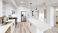 Located at 1921 Union St in Anaheim, California, this single-story home showcases a clean, contemporary design with a bright, neutral palette throughout. The kitchen serves as a standout centerpiece, featuring high-gloss white cabinetry, a large quartz island with pendant lighting, stainless steel appliances including a gas range, built-in microwave, dishwasher, and French door refrigerator, all complemented by a textured tile backsplash and recessed lighting. Light wood-look flooring flows through the main living and kitchen areas, enhancing the open, airy feel of the space. The living area is bright and welcoming, with natural light streaming through windows and a ceiling fan overhead. The bedrooms offer plush carpeting, ceiling fans, and windows with blinds, creating comfortable and restful retreats. The primary bathroom is particularly impressive, featuring a dual-sink vanity with white quartz countertops, black matte hardware, a large wall mirror, and a soaking tub, all set against light wood-look tile flooring. A secondary bathroom provides a single-sink vanity with the same refined finishes and convenient access to a walk-in closet. Throughout the home, black matte hardware and fixtures provide a consistent, modern accent that ties the design together cohesively.