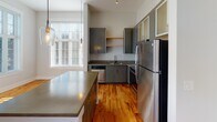 Located at 150 Coxe Ave in the heart of Asheville, NC, this single-floor unit offers a thoughtfully designed open-concept layout filled with natural light. Rich hardwood flooring flows seamlessly throughout the living areas and bedrooms, creating a warm and cohesive aesthetic.

The expansive living and dining area is anchored by large multi-pane windows and French doors that invite abundant daylight and offer views of the surrounding greenery. The space transitions naturally into a well-appointed kitchen featuring sleek gray cabinetry with frosted glass upper panels, open wood shelving, a full suite of stainless steel appliances, and a generous island with a concrete-style countertop — ideal for both cooking and entertaining.

The bedrooms are bright and comfortable, each finished with the same warm hardwood flooring and windows that bring in ample natural light. Closet access is conveniently positioned within the bedroom corridor.

The bathroom is finished with neutral large-format tile flooring, warm wood cabinetry, dual sinks with a wide vanity mirror, and a full soaking tub with tiled surround, offering a clean and functional design.

Throughout the unit, crisp white walls and clean architectural lines lend a modern, airy ambiance that complements the vibrant character of downtown Asheville.
