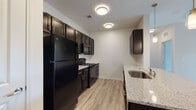 This single-floor residence offers a thoughtfully designed layout with modern finishes throughout. The kitchen is a standout feature, showcasing dark espresso cabinetry paired with granite countertops, a subway tile backsplash, and a full suite of black appliances including a refrigerator, gas range, and built-in microwave. A double stainless steel sink anchors the countertop workspace, and light wood-look flooring ties the space together seamlessly.

The open living and dining areas flow naturally from the kitchen, benefiting from recessed and pendant lighting overhead. A granite-topped peninsula provides additional surface space and subtly separates the kitchen from the dining area. The front entryway is visible from this zone, adding to the open, connected feel of the common spaces.

The bedrooms are generously sized, each featuring light wood-look flooring, ceiling fans, and ample natural light from windows dressed with horizontal blinds. At least one bedroom includes a walk-in closet with built-in shelving.

The bathrooms are finished with large-format tile flooring, dark vanity cabinetry with granite countertops, and wide mirrors with bright overhead lighting. The overall aesthetic is clean and contemporary, with neutral tones and consistent material choices creating a cohesive and comfortable living environment throughout.