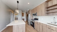 Located at 365 S Moorland Rd in Brookfield, Wisconsin, this thoughtfully designed three-bedroom, two-bathroom residence offers a clean, contemporary aesthetic across a single well-organized floor. Light wood-look flooring flows through the main living areas, drawing the eye from the hallway entry toward the open-concept kitchen, dining, and living room. The kitchen is a standout feature, equipped with warm wood-tone cabinetry, white quartz countertops, a subway tile backsplash, stainless steel appliances including a gas range and built-in microwave, and a center island illuminated by a stylish pendant light fixture. Open shelving adds both function and visual interest. Two balconies accessible via sliding glass doors provide outdoor living space with open views of the surrounding Brookfield landscape and autumn foliage. The three bedrooms are carpeted for comfort, each featuring generous closet space, including a walk-in closet with wire shelving. The bathrooms are finished with wood-tone vanities, quartz countertops, and clean white tile. A dedicated in-unit laundry area houses a full-size washer and dryer. Three closets throughout the home provide ample storage. The overall ambiance is bright, modern, and move-in ready.