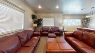This single-floor space combines functionality and comfort across its key areas. The kitchen is outfitted with light maple cabinetry, dark granite countertops, and black appliances, including a gas range with overhead microwave and a full-size refrigerator. A breakfast bar with a wood-paneled front provides a casual dining option, while pendant lighting and tile flooring complete the practical yet attractive design. Crown molding ties the space together seamlessly.

The living area exudes a warm, classic ambiance with neutral textured walls, crown molding, and recessed lighting. A corner gas fireplace with a wood mantel serves as a focal point, complemented by rich leather seating arranged around a wooden coffee table. A vibrant red area rug adds a bold accent, while multiple windows with blinds allow natural light to filter in, enhancing the welcoming atmosphere.

An adjoining open area extends the living space considerably and includes a full-size pool table, making it well-suited for entertaining. The layout flows naturally between the lounge seating and the game area, with additional windows providing ample daylight throughout. Together, these spaces create a cohesive, leisure-focused environment ideal for both relaxing and socializing.