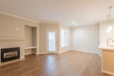This single-floor residence offers a thoughtfully designed layout that balances comfort and functionality throughout. The open living area serves as the heart of the home, showcasing rich hardwood-style flooring, crown molding, and a classic fireplace with a built-in niche — an ideal focal point for the room. A glazed exterior door and adjacent window flood the space with natural light, enhancing the warm, neutral color palette of the walls.

The kitchen is well-equipped with crisp white shaker-style cabinetry, a decorative tile backsplash, light wood-tone flooring, and a full suite of stainless steel appliances including a gas range, over-the-range microwave, and a French door refrigerator. A peninsula counter provides additional workspace and helps connect the kitchen to the main living area, where a stacked washer and dryer unit is also conveniently located.

The bedrooms feature plush carpeting, ceiling fans, and natural light from windows with exterior views. The primary bedroom is notably spacious, with dual mirrored sliding closet doors that add depth and brightness to the room.

The bathroom is cleanly finished with a white vanity, framed mirror, and a full tub-and-shower combination with built-in shelving. Hardwood-style flooring continues the cohesive design throughout this functional space.