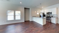 This two-story home combines modern finishes with a functional layout, highlighted by rich, dark hardwood flooring that flows consistently throughout both levels. The open-concept main living area connects seamlessly to the kitchen, which serves as a central hub of the home. The kitchen features white shaker cabinetry, granite countertops, a mosaic tile backsplash, and a full suite of stainless steel appliances including a gas range, microwave, and French door refrigerator. A peninsula with pendant lighting above provides additional counter space and casual seating. Recessed lighting and ceiling fans are found throughout the main level, contributing to a bright and well-ventilated atmosphere. Multiple windows allow natural light to filter into the living spaces. The bedrooms are generously sized, with select rooms boasting vaulted ceilings that amplify the sense of openness. The primary bedroom includes access to a dedicated bathroom and a walk-in closet. Both bathrooms are appointed with white vanities, granite countertops, and tub-shower combinations tiled in large-format marble-style tile. Additional built-in shelving in one bathroom provides practical storage. The overall aesthetic is clean, contemporary, and move-in ready.
