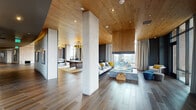 Located at 351 S Jackson St in Denver, CO, this elegantly designed single-floor space blends contemporary architecture with warm, natural materials to create an inviting and refined atmosphere. Throughout the interior, wide-plank hardwood flooring pairs seamlessly with richly toned wood-paneled ceilings, establishing a cohesive and sophisticated aesthetic.

The expansive main living area is anchored by a dramatic three-sided glass fireplace set on a concrete plinth, serving as a stunning architectural centerpiece that is visible from multiple vantage points. Floor-to-ceiling windows flood the space with natural light and frame panoramic views of the Denver skyline and surrounding cityscape, while floor-length linen drapes offer an elegant option for privacy.

A dedicated game and lounge area features a full-sized billiards table beneath a striking geometric pendant chandelier, complemented by a bold patterned area rug that adds a pop of color. The dining area accommodates intimate gatherings around a round dark-wood table, positioned directly beside expansive windows overlooking the city below.

Structural concrete columns punctuate the open-plan layout, lending an industrial contrast to the warmth of the natural wood surfaces. The entry corridor features dark matte walls, recessed lighting, and glass panel doors, offering a sleek transition into the main living space. The overall ambiance is modern, luxurious, and thoughtfully curated throughout.