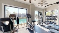 Located at 3114 Terry Brook Dr in Winter Park, FL, this 550-square-foot fitness center offers a well-equipped, single-floor workout facility designed to support a comprehensive exercise routine. The space features soaring ceilings with ceiling fans throughout, creating an open and airy atmosphere ideal for physical activity. Large windows on multiple walls flood the interior with abundant natural light while providing scenic views of the adjacent swimming pool and surrounding palm trees, bringing the Florida outdoors inside.

The fitness center is equipped with a diverse array of cardio machines, including multiple treadmills and a stair climber, as well as a full multi-station strength training machine, a dumbbell rack, various weight benches, and additional resistance equipment. Wall-mounted televisions provide entertainment during workouts. Durable rubber flooring covers the entire space, offering safety and stability underfoot.

Track lighting and pendant fixtures complement the natural light, ensuring the space remains bright at all times. A glass door provides direct access to the outdoor pool area. Fitness reference posters and a digital kiosk are also present, enhancing the functionality of the space. The clean, neutral color palette of light gray walls and white trim contributes to a modern, motivating workout environment.