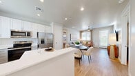 Located in San Tan Valley, Arizona, this thoughtfully designed single-story residence offers 2 bedrooms and 4 bathrooms within a well-utilized floor plan. The kitchen is a standout feature, showcasing two-tone cabinetry with white upper cabinets and gray lower cabinets, bright white quartz countertops, stainless steel appliances including a dishwasher and electric range, and a window above the sink that frames views of palm trees — a nod to the Arizona surroundings. Light wood-look flooring flows throughout the main living areas, complementing the clean, neutral palette.

The living room is bright and welcoming, with a large window allowing ample natural light and a glass door providing direct access to an outdoor area. The primary bedroom features light wood flooring, a ceiling fan, soft neutral walls, and a direct en-suite bathroom connection. The second bedroom is carpeted and well-lit by a large window with curtains. The four bathrooms include tub/shower combinations and clean white finishes. A dedicated laundry closet houses a stacked washer and dryer unit with overhead storage. Two closets provide additional storage throughout the home, making this a highly functional and modern living space.
