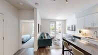 This thoughtfully designed 1-bedroom, 1-bathroom residence offers a contemporary open-concept layout that maximizes functionality and comfort. Wide-plank hardwood flooring runs throughout the main living areas, anchoring the bright, neutral palette that defines the space.

The kitchen is a standout feature, showcasing crisp white cabinetry with under-cabinet lighting, a marble-style island that doubles as a dining surface, stainless steel appliances including a gas range and French door refrigerator, and a subway tile backsplash. A stacked washer and dryer unit is conveniently integrated near the entry.

The living room is open and inviting, centered around a tufted teal sectional sofa and accented by a gallery wall of vibrant abstract artwork. Floor-to-ceiling sliding glass doors lead to a private balcony, filling the space with natural light and offering views of the surrounding community.

The bedroom provides a comfortable retreat with plush carpeting, dual windows, a large wall mirror, and a well-organized closet. The full bathroom features a wood-toned floating vanity, quartz countertop, undermount sink, and a tub-shower combination with tile surround. Clean lines and modern fixtures complete the refined, contemporary character of this well-designed residence.