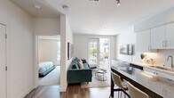 This thoughtfully designed 1-bedroom, 1-bathroom residence offers a contemporary open-concept layout that maximizes functionality and comfort. Wide-plank hardwood flooring runs throughout the main living areas, anchoring the bright, neutral palette that defines the space.

The kitchen is a standout feature, showcasing crisp white cabinetry with under-cabinet lighting, a marble-style island that doubles as a dining surface, stainless steel appliances including a gas range and French door refrigerator, and a subway tile backsplash. A stacked washer and dryer unit is conveniently integrated near the entry.

The living room is open and inviting, centered around a tufted teal sectional sofa and accented by a gallery wall of vibrant abstract artwork. Floor-to-ceiling sliding glass doors lead to a private balcony, filling the space with natural light and offering views of the surrounding community.

The bedroom provides a comfortable retreat with plush carpeting, dual windows, a large wall mirror, and a well-organized closet. The full bathroom features a wood-toned floating vanity, quartz countertop, undermount sink, and a tub-shower combination with tile surround. Clean lines and modern fixtures complete the refined, contemporary character of this well-designed residence.