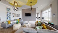 Located at 1105 E Twiggs St in the heart of Tampa, FL, this contemporary single-floor amenity space is designed to impress with bold colors, thoughtful design, and an open, airy layout. The main lounge area serves as the centerpiece, featuring multiple plush sectional sofas accented with vibrant yellow, teal, and green throw pillows arranged around distinctive natural stone stump coffee tables. A full-wall tile feature panel anchors a wall-mounted flat-screen TV, while a striking white ceiling with bold yellow circular accents and geometric pendant light fixtures adds dramatic visual interest overhead. Floor-to-ceiling windows line the perimeter, flooding the space with natural light and offering expansive views of the Tampa skyline and surrounding cityscape. A kitchenette area includes a vivid lime-green island with bar seating, pendant lighting, a sink, and a beverage refrigerator — ideal for social gatherings. A casual dining nook with a colorful geometric accent wall and built-in banquette seating provides an inviting spot to gather. The space also includes a game room area visible in the layout. Just beyond the interior, a private outdoor terrace is accessible through large glass doors, furnished with lounge chairs and seating, completing this dynamic and well-appointed communal environment.