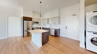 Located at 1600 Broadway in Sacramento's 95818 zip code, this modern 2-bedroom, 2-bathroom residence is thoughtfully designed with contemporary finishes throughout. The open-concept kitchen serves as the heart of the home, boasting two-tone cabinetry in rich dark wood and light gray, quartz countertops, a central island, stainless steel appliances, and warm hardwood-style flooring — all beneath soaring ceilings that lend an airy, expansive feel.

Both bedrooms feature plush carpeting, clean white walls, and sliding or panel-style closets. The primary bedroom opens to a private balcony through full-height glass sliding doors, offering bright natural light and views of mature trees. Each bedroom is also equipped with a ceiling fan for added comfort.

The two bathrooms are finished with large-format tile flooring and textured tile surrounds. One features a walk-in shower with mosaic tile flooring and a backlit vanity mirror, while the second includes a soaking tub with a handheld shower and is conveniently located adjacent to a stacked in-unit washer and dryer. This well-appointed residence combines modern aesthetics with practical amenities in a cohesive, move-in-ready layout.