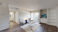 This single-story residence offers a thoughtfully designed layout with a neutral color palette and a blend of hardwood-style and carpeted flooring throughout. The living area is the centerpiece of the home, featuring rich dark wood-look flooring, textured walls, and a large sliding glass door flanked by vertical blinds that flood the space with natural light and provide access to an outdoor area. A built-in shelving unit and white cabinetry add both function and visual interest to the living space.

The kitchen is well-equipped with white shaker-style cabinetry, granite countertops, a stainless steel sink, a subway tile backsplash, and a stainless steel electric range with an overhead exhaust hood, delivering a clean and modern aesthetic.

The bedroom is generously sized, highlighted by dual windows that bring in ample natural light, plush carpet flooring, and a ceiling fan. An adjoining walk-in closet provides substantial storage with multiple shelving units and hanging rods on three walls.

The bathroom is clean and functional, featuring a full tub-shower combination with a grab bar, wood-look tile flooring, and a curtained shower surround. Overall, the space maintains a bright, neutral ambiance throughout.