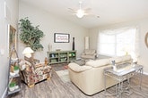 This single-floor residence offers a well-designed layout that balances functionality and comfort throughout its main living spaces. The kitchen is a standout feature, outfitted with crisp white shaker-style cabinetry, granite countertops, a classic white subway tile backsplash, and a full suite of stainless steel appliances including a refrigerator with ice and water dispenser, electric range, over-the-range microwave, and dishwasher. Wood-look flooring runs through the kitchen and extends into the open living and dining areas, creating a cohesive flow. The living room is bright and welcoming, anchored by a bay-style window that draws in natural light and is fitted with a ceiling fan overhead. The dining area sits adjacent, illuminated by a chandelier fixture. The bedrooms feature plush carpeting, ceiling fans, and windows providing natural light; closet access is visible in the primary bedroom. The bathroom is clean and straightforward, featuring tile flooring, a walk-in shower unit, and white fixtures. Neutral wall tones throughout contribute to a light, airy atmosphere that complements the space's practical and comfortable design.
