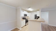 Located at 4911 Signature Dr in Myrtle Beach, South Carolina, this single-floor residence offers a well-organized, open-concept layout designed for comfortable everyday living. The kitchen is a functional highlight, featuring white cabinetry, light granite-style countertops, stainless steel appliances including a range, microwave, refrigerator, and dishwasher, and light wood-look flooring. A peninsula with a breakfast bar connects the kitchen to the adjacent dining and living areas, creating a seamless flow throughout the main living space. The living area is generously proportioned, finished with the same light wood-look flooring, crown molding, and a ceiling fan, with vertical blinds providing access to natural light. Bedrooms are carpeted and bright, each equipped with ceiling fans and multiple windows that invite natural light and outdoor views. The bathrooms are clean and consistent in design, featuring white vanities with granite-style countertops, large mirrors, and light wood-look flooring. A second full bathroom includes a tub-shower combination. Throughout the home, a neutral color palette, textured ceilings, and crown molding details contribute to a cohesive and inviting ambiance.