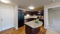 This single-floor residence at 8601 Edinbrook Crossing in Brooklyn Park, Minnesota, offers a thoughtfully designed layout with a cohesive blend of warm tones and practical finishes throughout. The kitchen is a standout feature, boasting rich dark cabinetry, granite countertops, a curved island, hardwood-style flooring, and stainless steel appliances, including a range, microwave, and dishwasher. The open sight line from the kitchen to the living area creates a connected, functional flow ideal for everyday living. The living area is generously proportioned, featuring plush carpeting, neutral walls, a textured ceiling, and a large window alongside a exterior door that invites natural light and outdoor access. The bedrooms are comfortably sized, each with soft carpet flooring, windows with blinds, and clean white trim. Two bathrooms serve the unit: one features a tub-shower combination with a stylish curtain, dark vanity cabinetry, granite countertops, and tile flooring, while the second bathroom includes a walk-in shower with glass enclosure and a matching dark vanity with granite countertop. The overall ambiance is clean, modern, and move-in ready, with consistent warm neutral tones and quality finishes that lend a welcoming feel throughout the space.