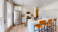 Located at 2020 Winters Eve Dr in Charlotte, NC, this thoughtfully designed single-floor residence offers 2 bedrooms and 2 bathrooms across a comfortable and functional layout. The open-concept living, dining, and kitchen area serves as the heart of the home, bathed in natural light from large windows dressed with linen curtains and blinds. The living room features light hardwood-style flooring, a ceiling fan, and a warm, inviting ambiance that flows seamlessly into the dining area, which is framed by corner windows offering pleasant outdoor views. The kitchen is well-equipped with white shaker cabinetry, stainless steel appliances including a French door refrigerator and microwave, a white quartz-topped island with bar seating, and a sleek matte black faucet. The primary bedroom features a bold accent wall and cozy carpeting, while the second bedroom offers a ceiling fan, plush carpet, and a bright window with neighborhood views. Both bathrooms are clean and modern, with one featuring a tiled tub-shower combo and matte black fixtures. A dedicated in-unit laundry room with wire shelving adds everyday convenience. Two closets and a hallway complete this well-rounded and move-in-ready home.