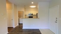 This single-floor residence is designed with an open, functional layout that seamlessly connects the living area to the kitchen. The kitchen is outfitted with white shaker-style cabinetry that extends to the upper walls, providing ample storage space. A tile backsplash adds a clean, classic detail behind the stainless steel appliances, which include a built-in microwave, an electric range, and a full-size refrigerator. The peninsula-style breakfast bar extends from the kitchen, creating a natural division between the cooking and living spaces while offering additional seating and counter space.

Dark hardwood-style flooring runs throughout the main living area, offering a rich contrast to the bright white walls and cabinetry. Recessed and flush-mount ceiling lighting provides consistent illumination throughout the space. A dedicated laundry area is conveniently tucked just off the kitchen, housing a full-size washer and dryer unit with built-in shelving above. The overall aesthetic is clean and neutral, with a practical, well-organized layout suited for everyday living.