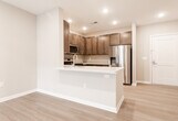 Located at 23 US-1 S in New Brunswick, NJ, this well-appointed single-floor residence showcases a thoughtfully designed open-concept layout with contemporary finishes throughout. The kitchen is a standout feature, equipped with rich dark-wood cabinetry, stainless steel appliances including a gas range, microwave, and refrigerator, complemented by crisp white quartz countertops and a neutral tile backsplash. A peninsula with an integrated sink extends the workspace and creates a natural connection to the living area, which is finished with light wood-style flooring. The expansive living space benefits from recessed lighting and a tray ceiling detail, with sliding glass doors opening to a private balcony that invites natural light. The bedroom continues the tray ceiling design and features soft carpeting and a bright window. The primary bathroom is generously sized, offering a dual-sink vanity with dark wood cabinetry, a large framed mirror, light tile flooring, and a glass-enclosed walk-in shower with subway tile surround. Clean white walls and warm neutral tones create a cohesive, modern ambiance throughout the residence, making it a polished and functional living space.